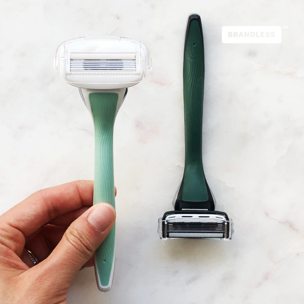 Lifestyle photo, a woman holds up the razor for body next to a razor for face sitting on a bathroom countertop.