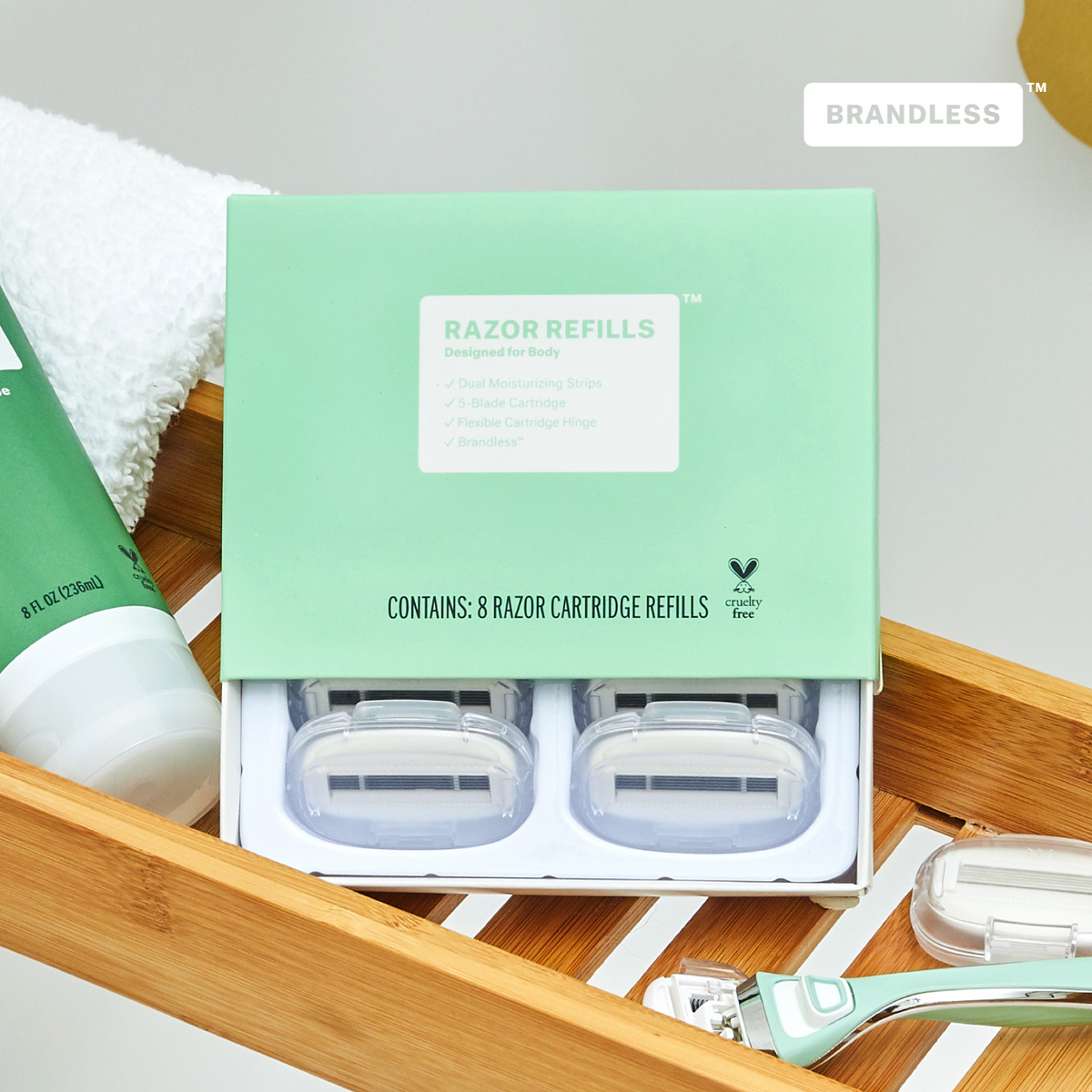 Lifestyle photo, razor refills for body, box slightly open and showing the razor refill cartridges, box sits in a bamboo shower caddy next to a razor for body and a tube of green tea and aloe shave gel. 