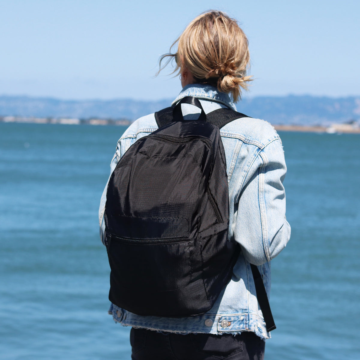 Lifestyle photo of a woman on the coast with the Brandless foldable backpack on her back.