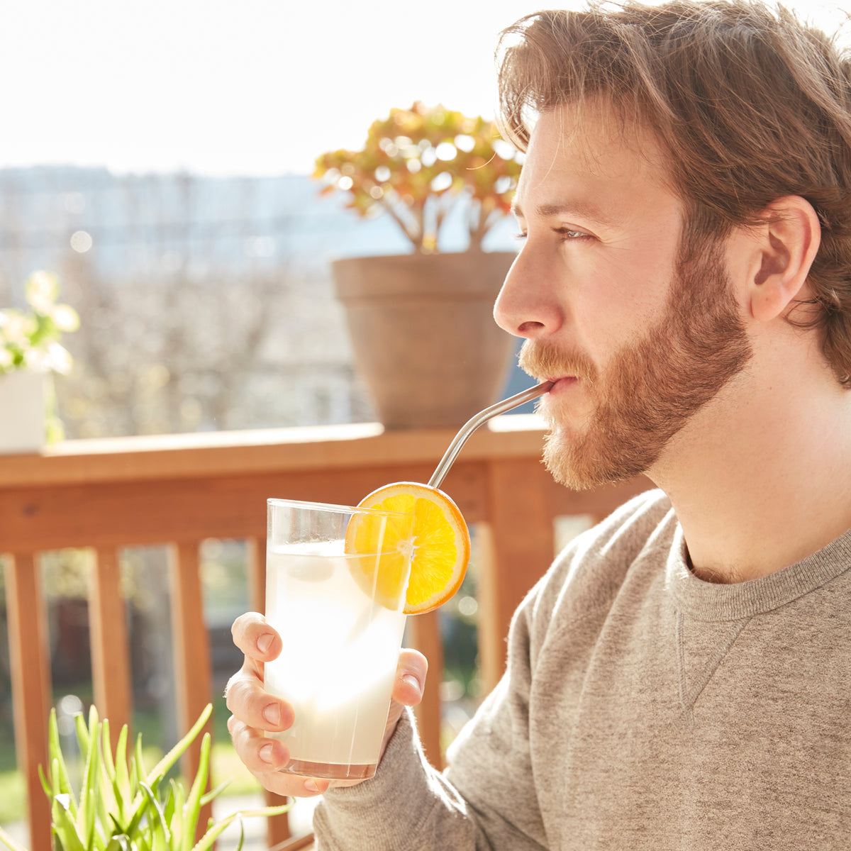 Lifestyle photo, man enjoys a summertime lemonade from a tall glass tumbler with a fresh orange slice using a brandless stainless steel straw.