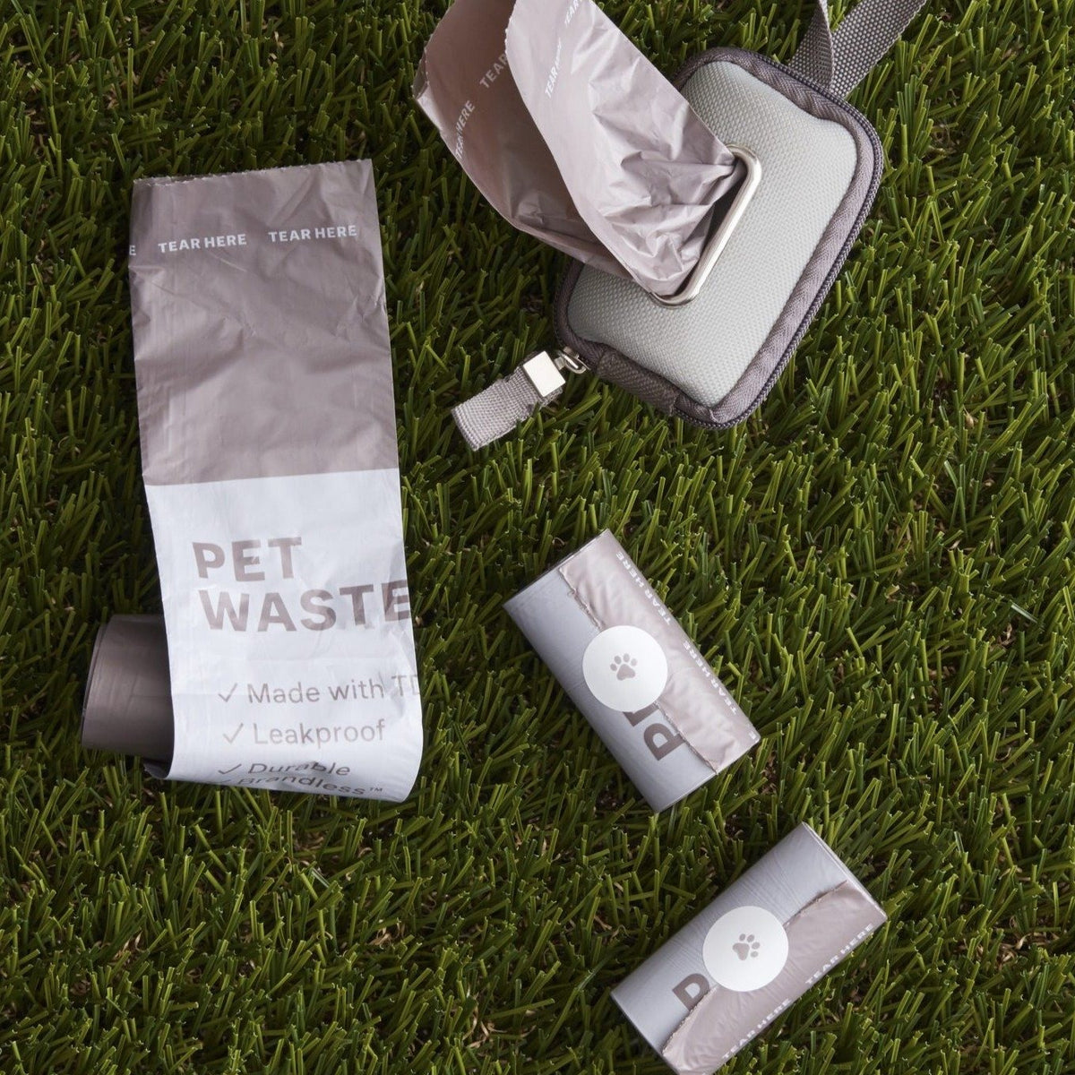 Lifestyle photo, showing the brandless pet waste bag rolls and waste bag dispeser on grass.