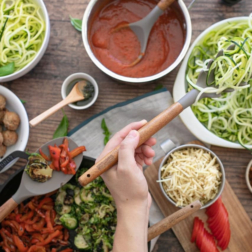 Man's hand serves up some fresh zoodles from a bowl with the brandless silicone pasta server.