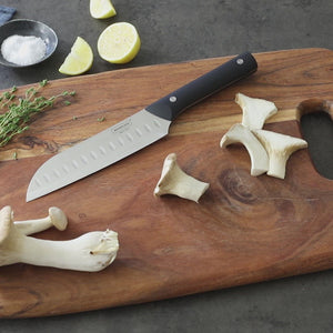 Video.  Man's hands demonstrating a push-down-and-quarter-slide-forward slicing technique with the santoku knife on some long-stalk mushrooms on a cutting board with quartered lemons and coarse salt in the background.