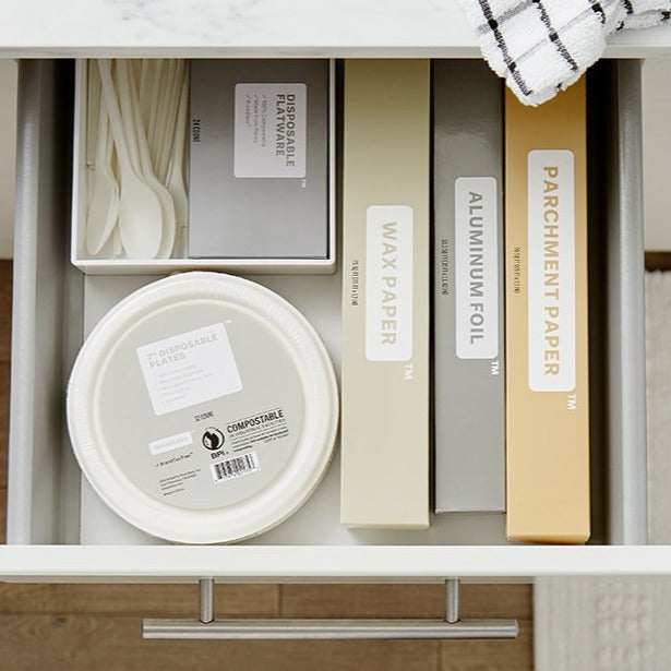 Lifestyle photo, showing Brandless&#39;s line of kitchen baking accessories: parchment paper, aluminum foil, wax paper, tree-free paper plates, and disosable flatware all stored neatly in a kitchen drawer.