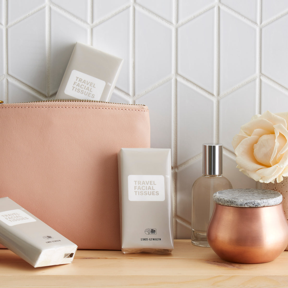 Lifestyle, travel facial tissue packs lean against a purse on a bathroom shelf next to a perfume bottle and a single rose in a cup-sized vase.in preparation for an evening out.
