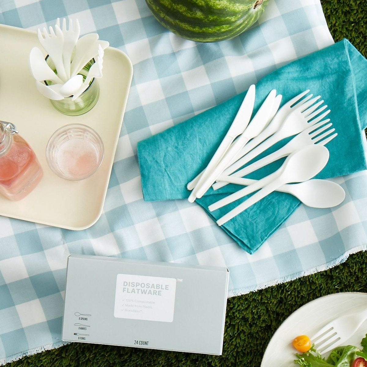 Lifestyle photo of disposable flatware laid out on a napkin at a lawn picnic.
