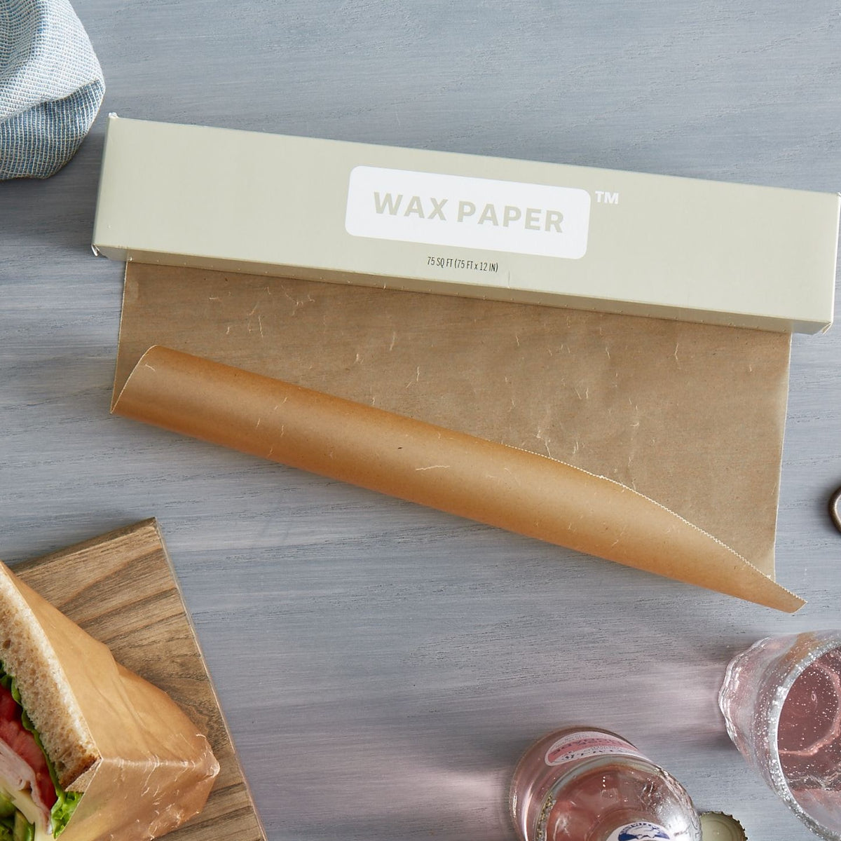 Lifestlye photo of wax paper being unrolled on a kitchen counter next to sandwiches.