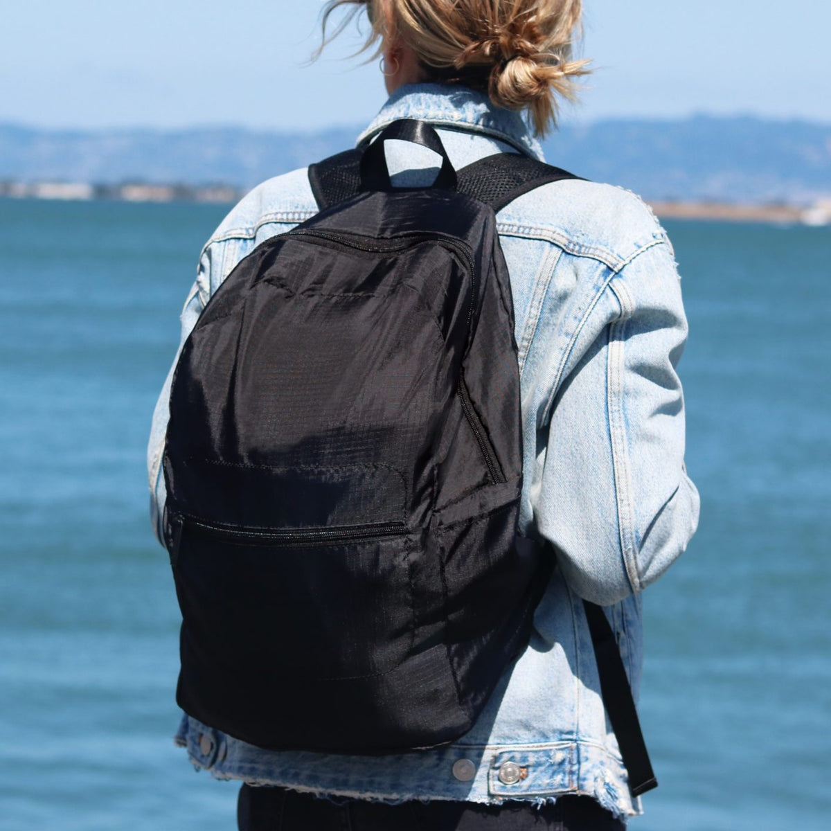 Lifestyle photo of a woman on the coast with the Brandless foldable backpack on her back.