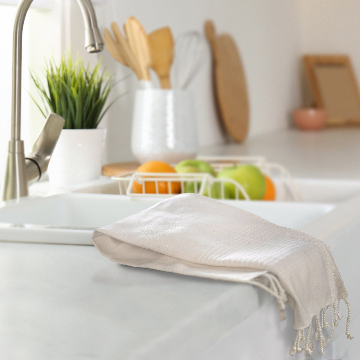 Lifestyle photo of organic cotton towel in natural color sitting folded next to a kitchn sink.