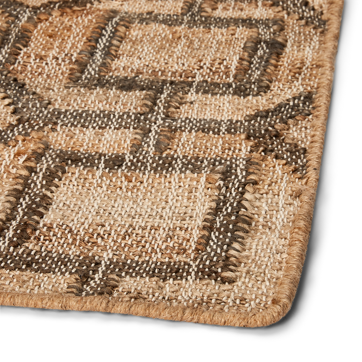 Detail view of rug corner, showing fully stitched and rounded corner, consistent weave, and blend of natural earthtone colors.