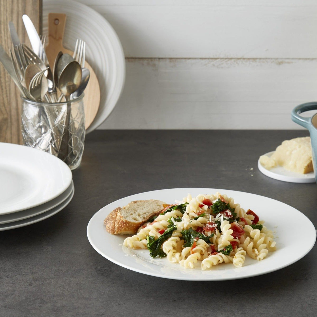 Lifestyle. Kitchen counter, with chef plating a gorgeous kale and tomato pasta dish on a white porcelain dinner plate.