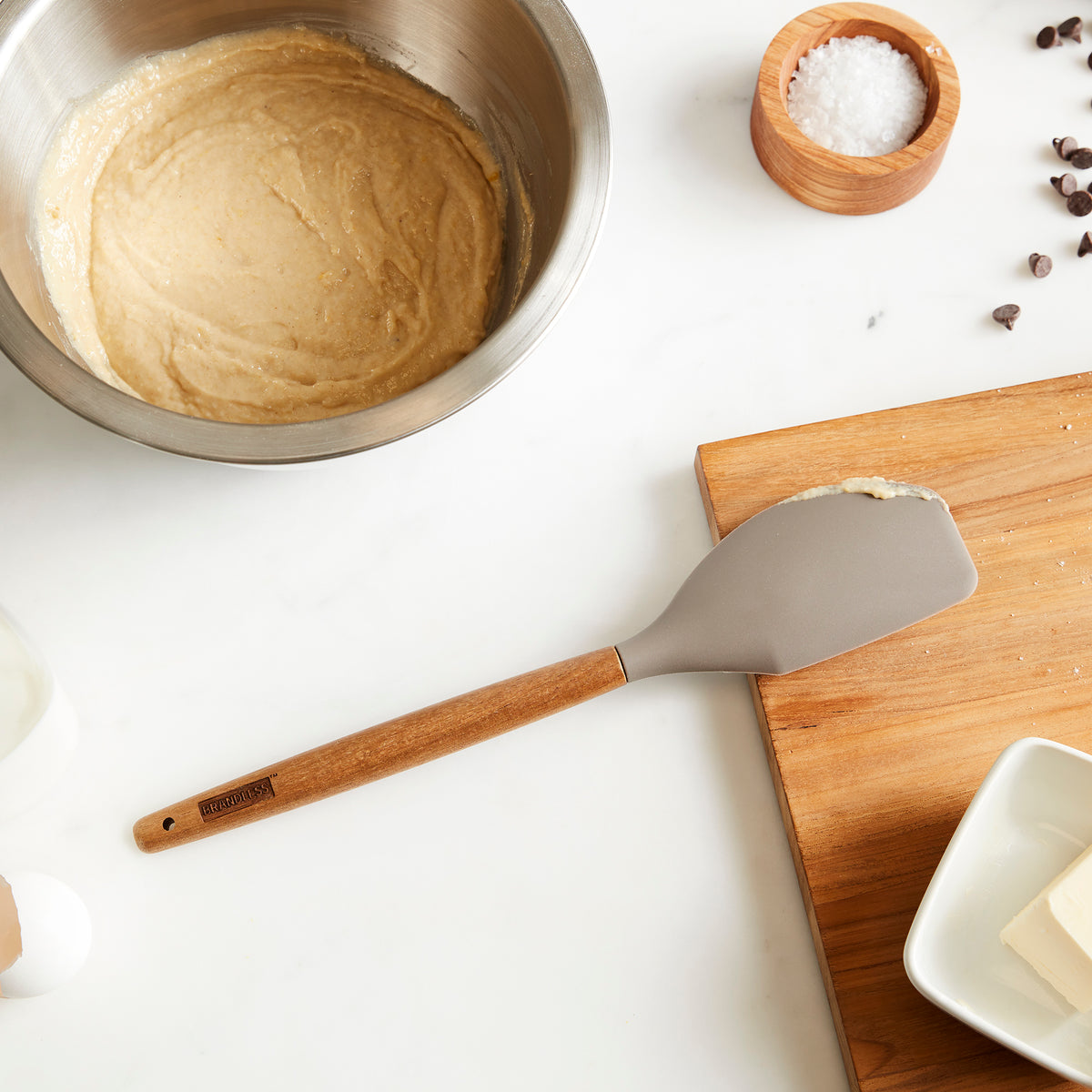 Lifestyle photo, silicone spatula with vestiges of cake batter rests on cutting board next to a mixing bowl full of cake batter.
