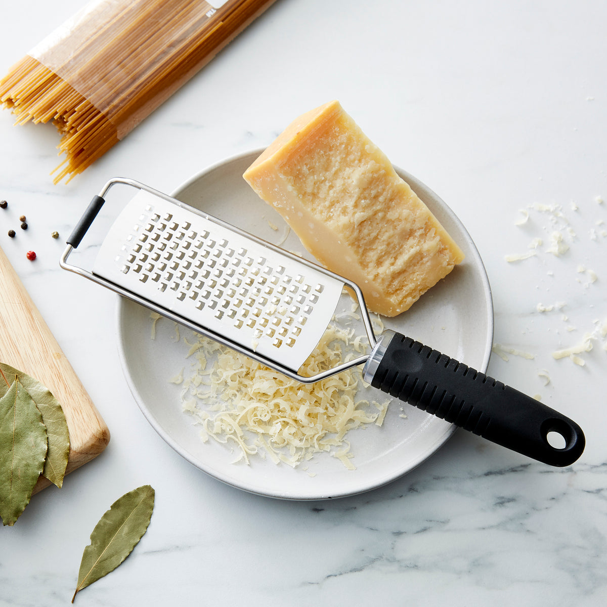 Lifestyle photo, cheese grater on a plate with a hard aged Parmesean cheese block.