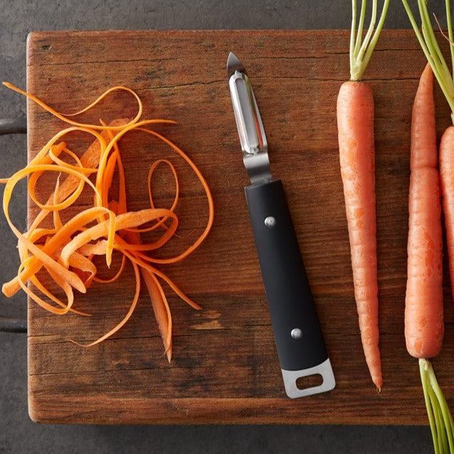 Lifestyle, vegetable peeler next to fresh carrots from the garden and nice uniform peels from a carrot on a cutting board.