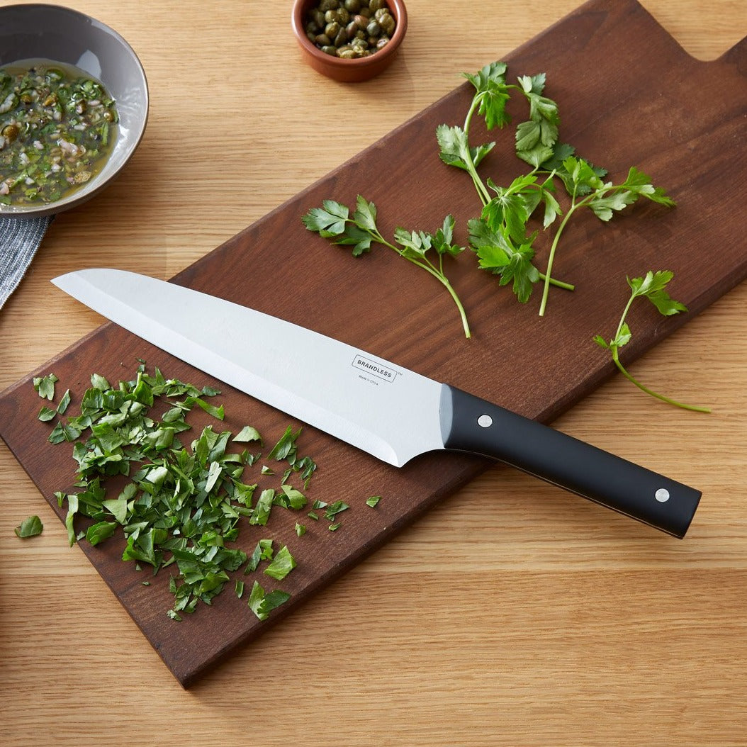 Lifestyle photo, 8 inch chef&#39;s knife laying on a cutting board with minced parsley.