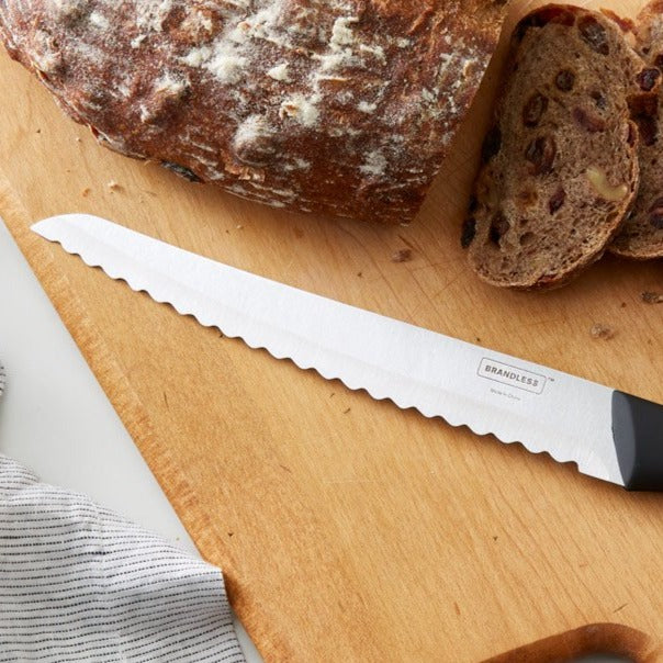 Brandless 8 inch bread knife laying on a cutting board next to a loaf of sliced bread.