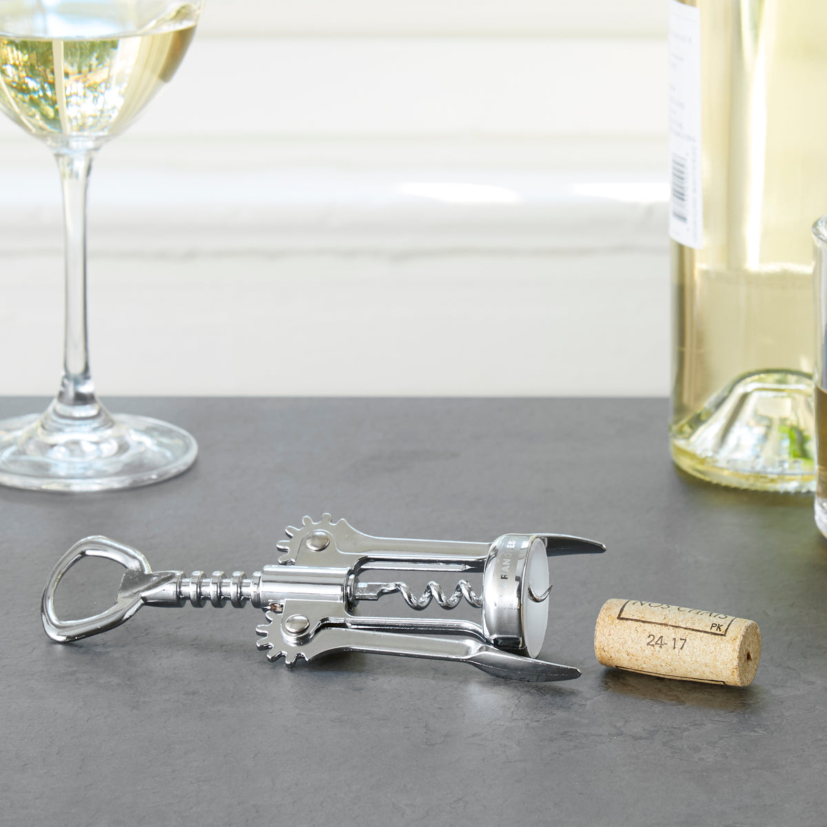 Lifestyle photo, corkscrew on a counter next to a cork, having just been removed from a bottle of white wine.