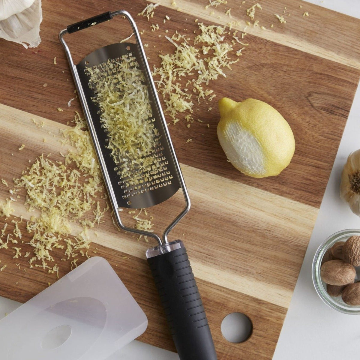 Lifestyle photo, fine cheese grater being used on a fresh lemon skin to create easy, consistent, and aromatic lemon zest on a cutting board.