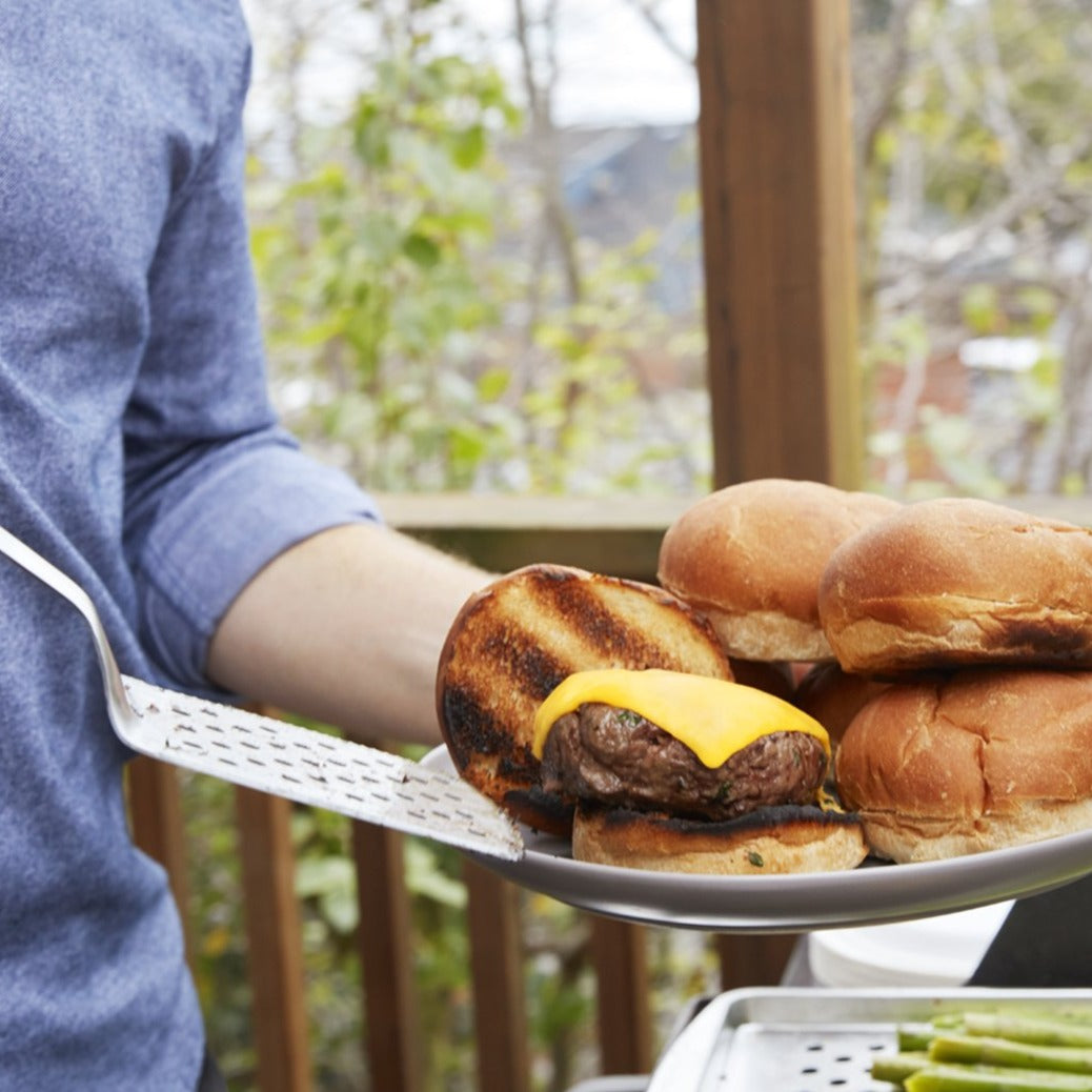 Lifestyle photo. A man uses a grill spatula to serve a fresh hamburger from a platter to a plate.