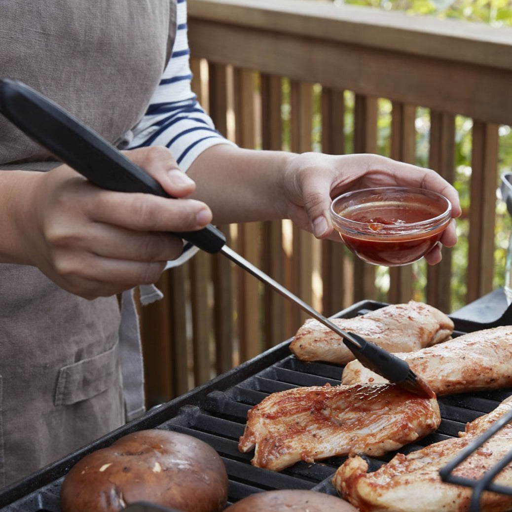 Lifestyle photo, man applying barbeque sauce to pieces of chicken on a grill next to some grilled mushroom caps.