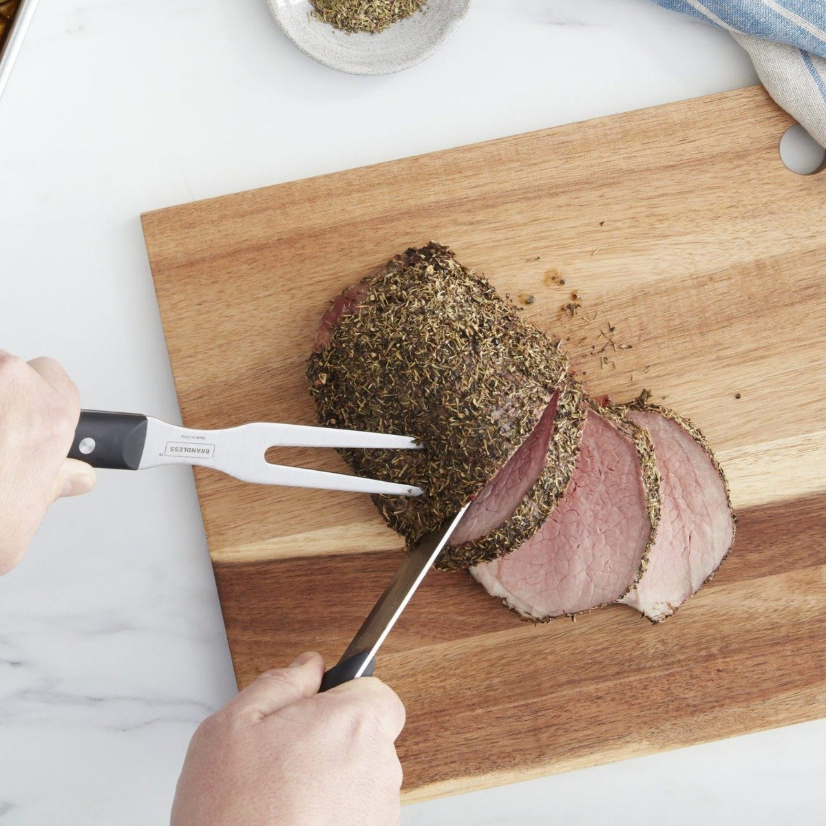 Lifestyle photo, a man&#39;s hands using a carving knife and carving fork to neatly slice a pork loin on a cutting board.