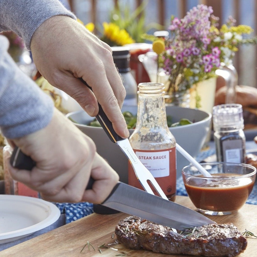 Lifestyle photo, man&#39;s hands holding carving knife and carving fork and slicing into a steak on a cutting board.