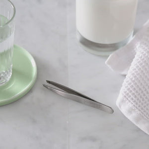 Video, no sound. Woman picks up tweezers from a marble bathroom countertop and demonstrates the ease with which the precision slant tweezers can be grasped firmly and compressed easily to make tweezing in any area simple and fast.