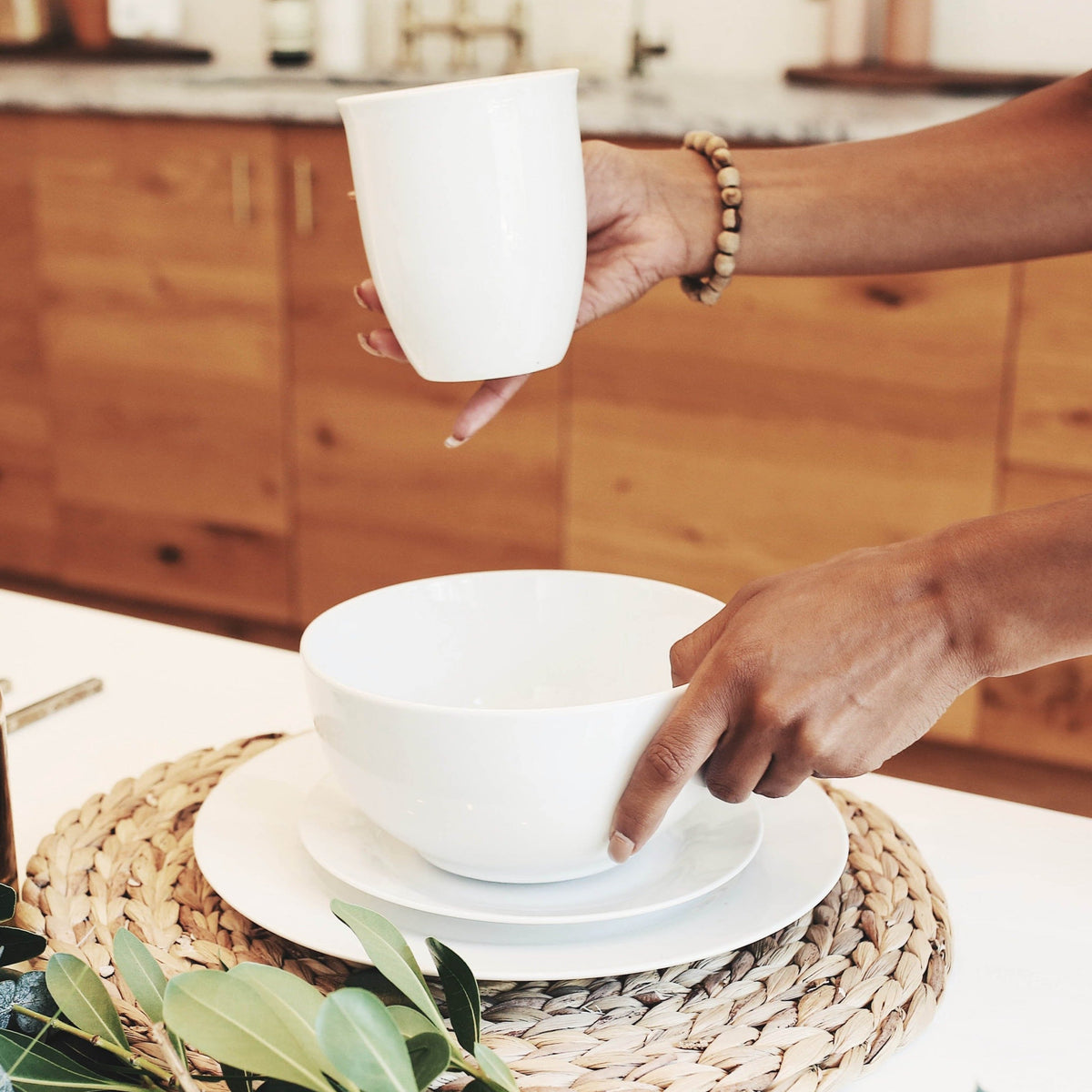 Lifestyle, woman places a white porcelain coffee mug onto a beautifully decorated dining room table complete with stacked white porcelain bowl and plates.