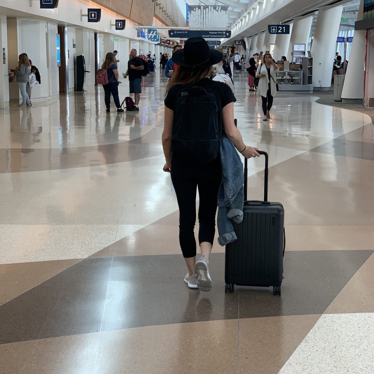 Lifewstyle photo of a woman walking through an airport with a brandless wheeled luggage bag.