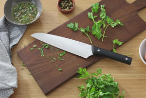 Video of a woman's hands using the 8 inch chef's knife to cut parsley on a cutting board.