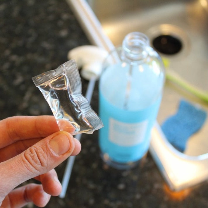 Lifestyle photo, woman inserts a cleaning pack into an empty refillable multi surface cleaner bottle.  Once inserted, she&#39;ll add 32oz of tap water to create a whole new bottle full of multi surface cleaner.