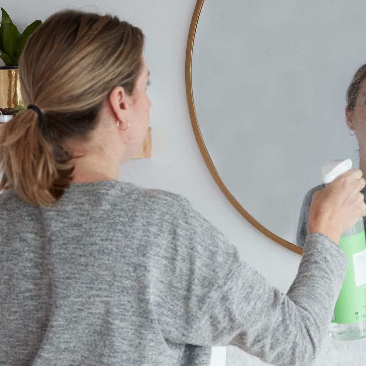 Lifestlye photo, a woman sprays a mirror with non-toxic cucumber mint glass cleaner.